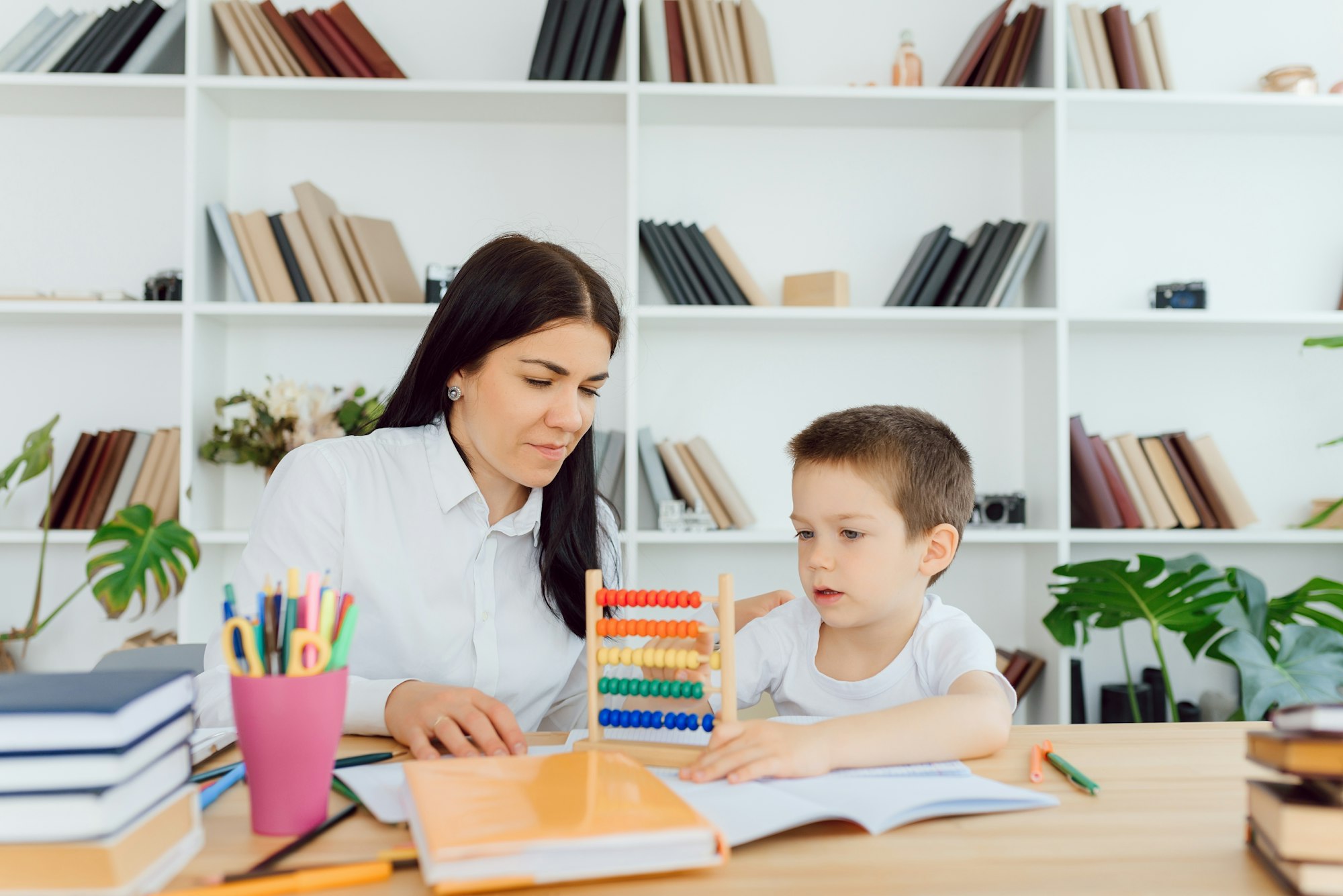 Young female tutor helping little elementary school boy with homework during individual lesson